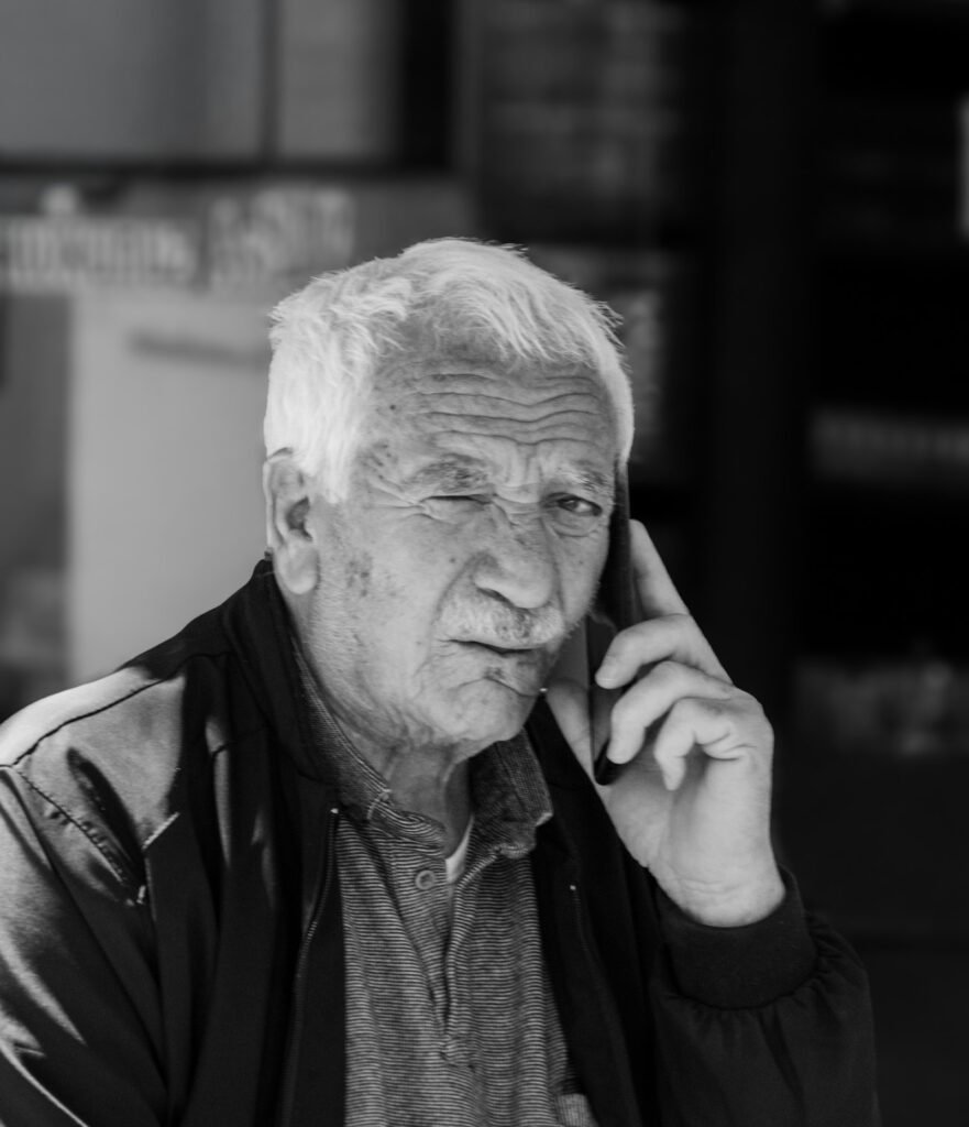 Senhor idoso de cabelo branco falando ao celular, com expressão séria.